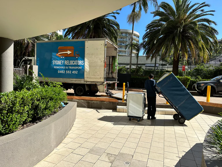 Appliances and wrapped furniture staged in an apartment forecourt beside the truck