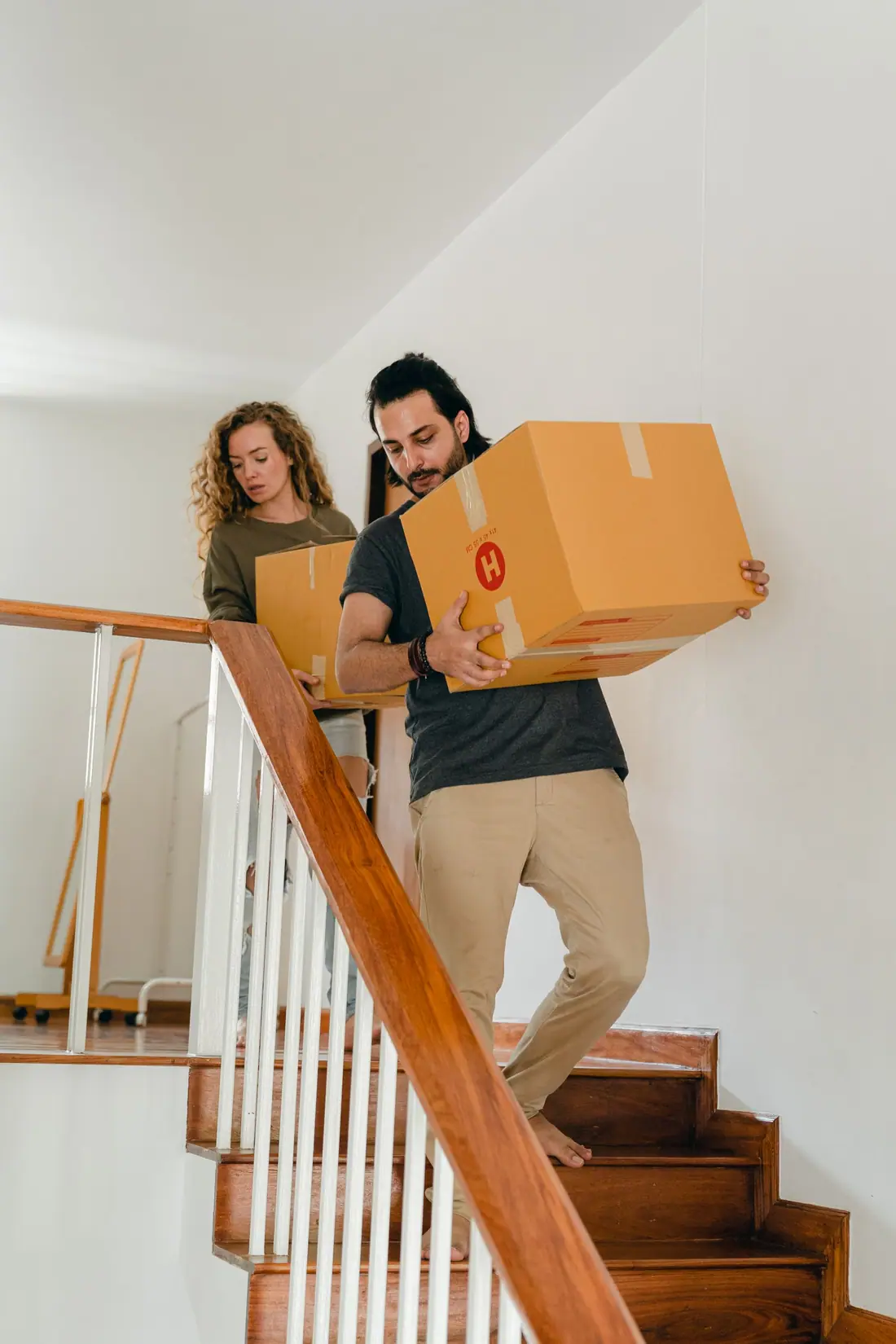 Two people carrying boxes down a staircase together