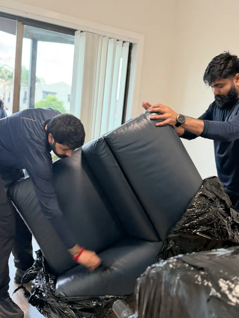 Crew carrying upholstered furniture by hand, fully wrapped