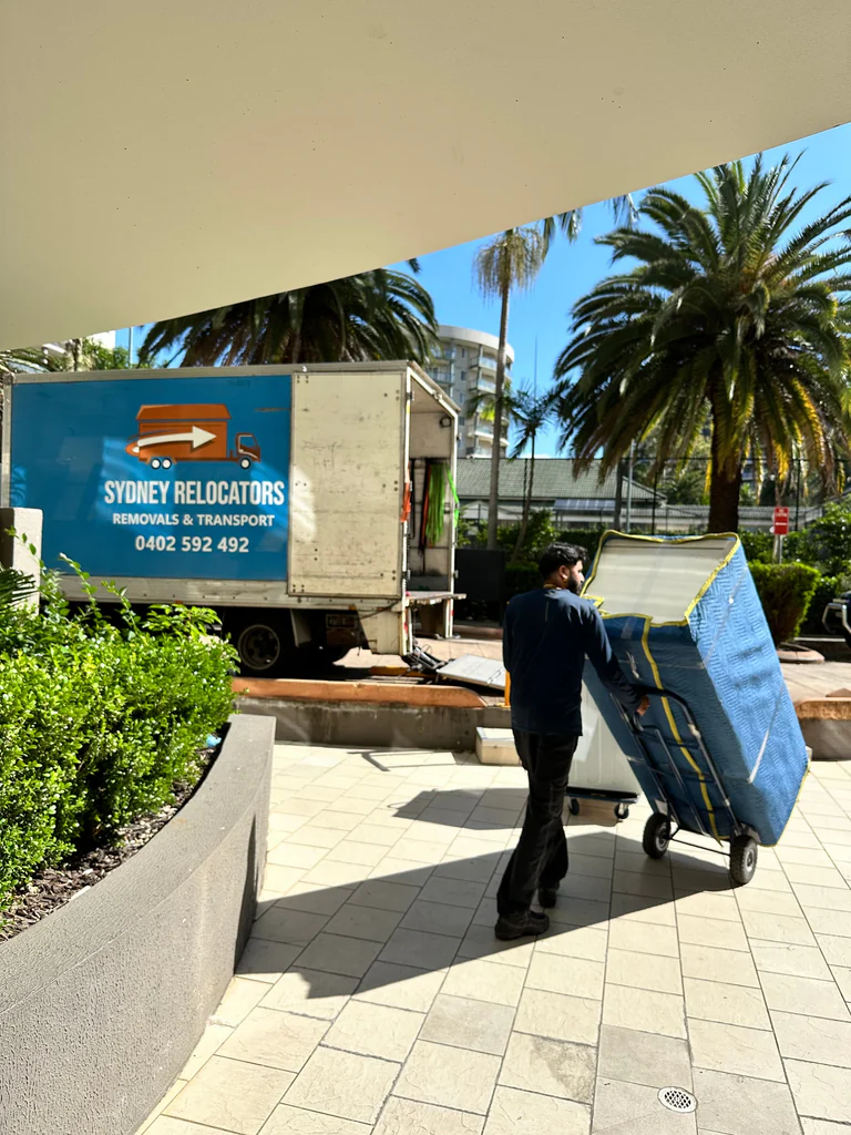 A blanket-wrapped mattress wheeled out to the truck on a trolley
